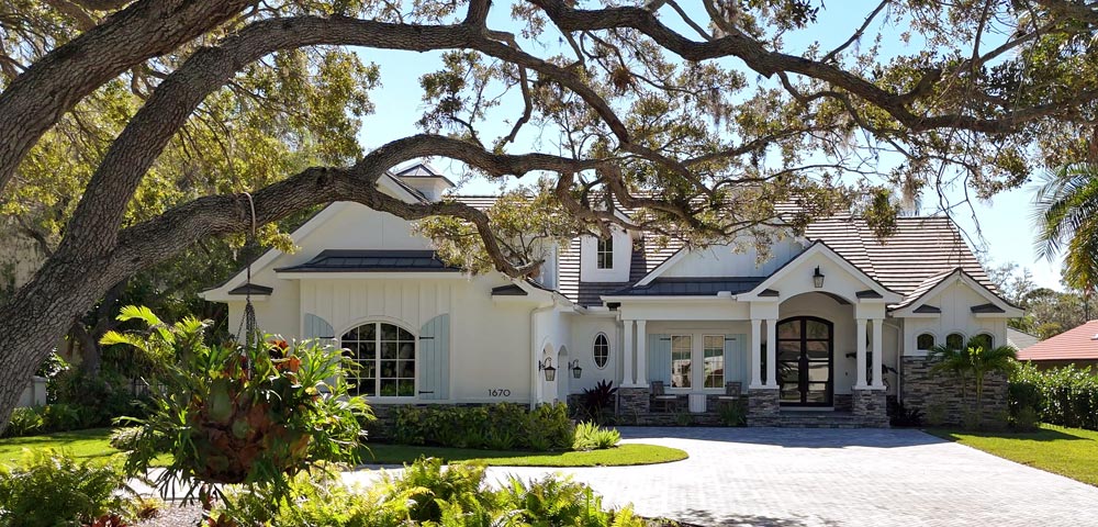 Street view of white modern coastal farmhouse style single family home with light blue shutter accents and large live oak tree